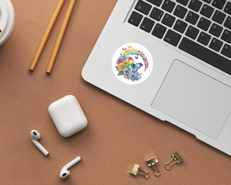 May include: A watercolor sticker featuring a butterfly with rainbow wings and flowers. The butterfly is perched on a rainbow arc. The sticker is on a white background.