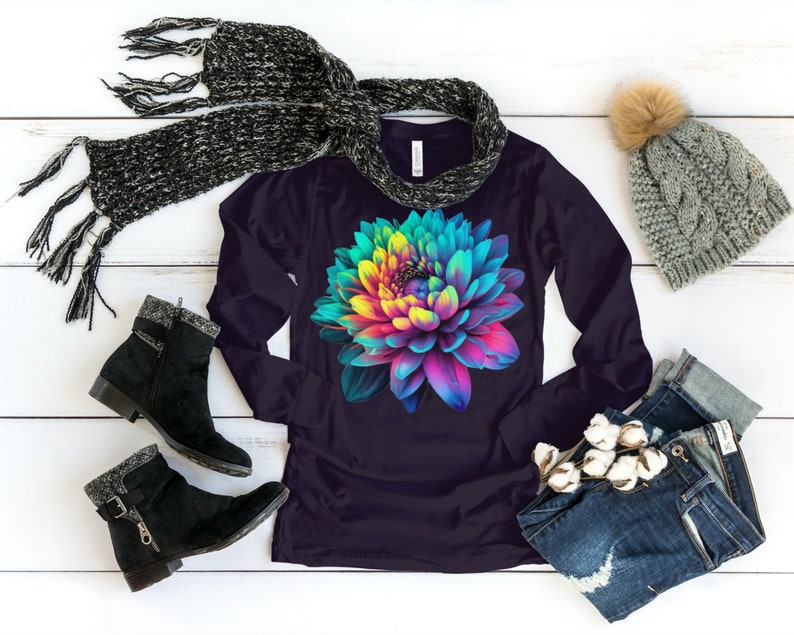 May include: A long-sleeved shirt with a colorful flower graphic on a dark purple background. The shirt is shown with a scarf, a beanie, and jeans.