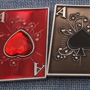 May include: Two metal playing card charms, one red with a red gem heart and the other black with a black spade. Both charms feature the letter 'A' and ornate designs.
