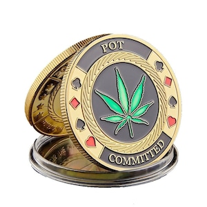 May include: Gold-colored metal coin with a black and green marijuana leaf design. The coin has the words "POT COMMITTED" around the edge and four playing card suits in the corners.