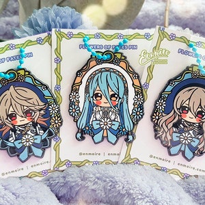 May include: Three enamel pins featuring anime-style characters with blue, white, and pink accents. Each pin is shaped like an oval and has a floral border. The pins are attached to chains and have the text "Flowers of Fates Pin" on the card.