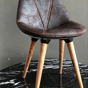 May include: A brown upholstered chair with a distressed leather look. The chair has a curved back and is supported by four wooden legs. The legs are angled and have a natural wood finish. The chair is designed for seating.
