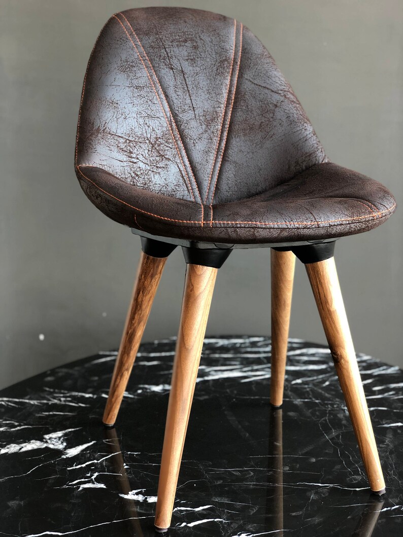 May include: A brown upholstered chair with a distressed leather look. The chair has a curved back and is supported by four wooden legs. The legs are angled and have a natural wood finish. The chair is designed for seating.