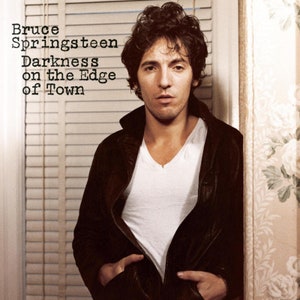 May include: A black and white album cover featuring Bruce Springsteen. The album title is "Darkness on the Edge of Town".