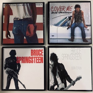May include: Four black framed album covers with white backgrounds. The covers feature Bruce Springsteen and the album titles "Born in the USA", "Cover Me", "Bruce Springsteen", and "Born to Run".