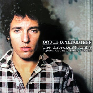 May include: A black and white checked shirt worn by Bruce Springsteen, with the text "BRUCE SPRINGSTEEN The Unbroken Promise Lighting Up The Darkness Sessions" on a black background.