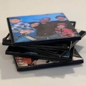 May include: A stack of black photo coasters with images of a family. The top coaster features a group of people, including a child wearing a red shirt with the word "Junior" on it.