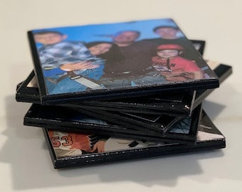 May include: A stack of black photo coasters with images of a family. The top coaster features a group of people, including a child wearing a red shirt with the word "Junior" on it.
