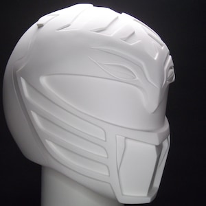 Può includere: Casco in plastica bianca con un design dettagliato, che ricorda un elmo da guerriero. Il casco ha un design angolare rialzato con una visiera prominente.