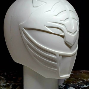 Può includere: Casco in plastica bianca con un design dettagliato, che ricorda un personaggio di un popolare programma televisivo. Il casco è su un supporto bianco.