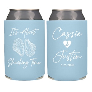 May include: Two light blue can coolers. One cooler has the text "It's About Shucking Time" with oyster illustrations. The other cooler has the names "Cassie & Justin" with a heart symbol and the date "5.25.2028".