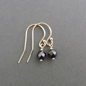 May include: A pair of gold-colored earrings with black, faceted gemstone beads. The earrings have a simple hook design and a small, round bead at the top of the hook. The gemstones are approximately 0.25 inches in diameter.