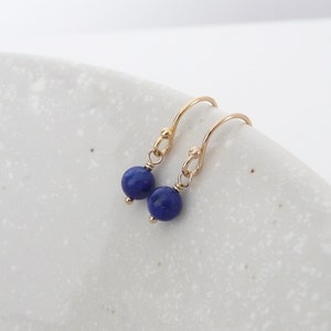 May include: A pair of gold earrings with small, round, dark blue lapis lazuli stones.