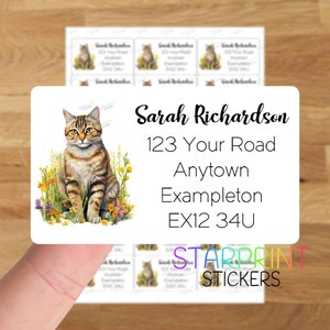Peut inclure: Un autocollant rectangulaire blanc avec une illustration de chat tigré et le texte "Sarah Richardson, 123 Your Road, Anytown Exampleton, EX12 34U". L'autocollant a une bordure florale verte, jaune et blanche.
