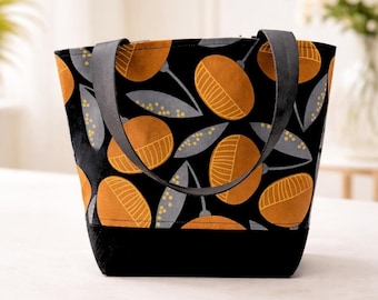 May include: Black tote bag with a repeating pattern of orange and yellow stylized fruit or flower shapes on a black background. The bag has a solid black base and gray handles.