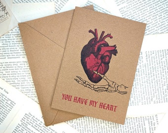 May include: Kraft paper greeting card with a red anatomical heart illustration and a skeleton hand. The text "YOU HAVE MY HEART" is printed in red. Includes a matching envelope. Perfect for Valentine's Day or a romantic occasion.