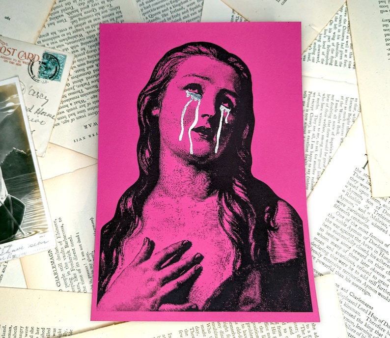 Puede incluir: Una impresi&oacute;n art&iacute;stica rosa con una ilustraci&oacute;n en blanco y negro de una mujer con l&aacute;grimas. Las l&aacute;grimas est&aacute;n resaltadas con pintura blanca. La mujer mira hacia arriba con la mano en el pecho. El fondo es rosa.