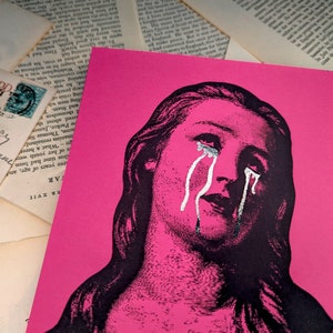 Puede incluir: Una impresi&oacute;n art&iacute;stica rosa con una ilustraci&oacute;n en blanco y negro de una mujer llorando. Las l&aacute;grimas est&aacute;n resaltadas en plata. La imagen est&aacute; rodeada de postales antiguas y p&aacute;ginas de libros.