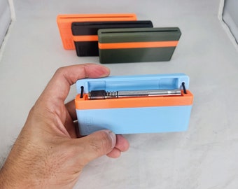 Peut inclure: Un étui rectangulaire bleu clair et orange contenant un objet métallique argenté. L'étui est ouvert, révélant le contenu. Deux autres étuis orange, noirs et vert olive sont en arrière-plan.