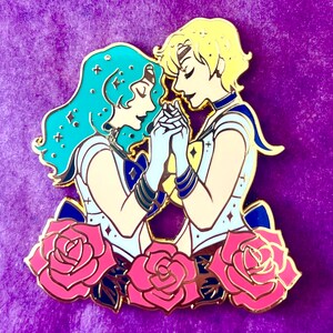 Puede incluir: Pin de esmalte dorado con dos personajes de anime, uno con cabello azul y el otro con cabello rubio, tomados de la mano y rodeados de rosas rosas.