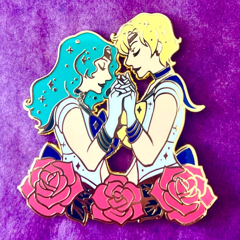 Puede incluir: Pin de esmalte dorado con dos personajes de anime, uno con cabello azul y el otro con cabello rubio, tomados de la mano y rodeados de rosas rosas.