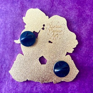 Puede incluir: Pin de metal de color dorado con la silueta de dos personas abraz&aacute;ndose. La parte posterior del pin tiene dos cierres met&aacute;licos y el texto "Karina Moreno Art".