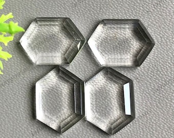 以下が含まれることがあります： ファセットエッジのある透明なガラスの六角形のcabochonsが4つ。cabochonsは、グレーのテクスチャのある表面に半円形に配置されています。