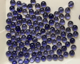 May include: A large group of round, purple gemstones, with a slight gradient of color from light to dark purple. The gemstones are arranged in a random pattern on a white surface.