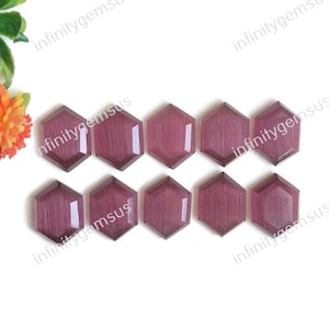 Puede incluir: Diez piedras preciosas hexagonales y facetadas, de color ciruela oscuro, están dispuestas sobre una superficie blanca. Las gemas tienen un aspecto pulido y están talladas con múltiples facetas. Las piedras preciosas son probablemente para la fabricación de joyas o manualidades.