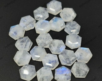May include: A collection of 17 white hexagonal moonstone cabochons with iridescent rainbow flashes. The stones are smooth and polished, with a slightly rounded shape.