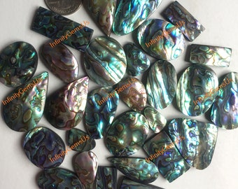 Könnte beinhalten: Sortiment aus irisierenden Abalone-Muschel-Cabochons in verschiedenen Formen und Größen. Die Cabochons haben eine blaue, grüne und violette Farbe mit einem Perlmutt-Glanz.