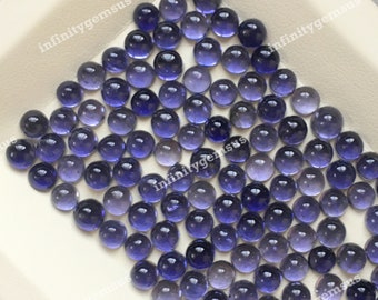 May include: A collection of round, purple and clear gemstone cabochons. The cabochons are smooth and polished, with a slight shimmer.