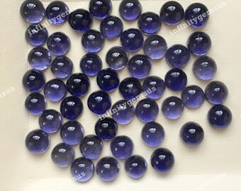 May include: A collection of round, polished gemstones in varying shades of deep blue and purple. The gems are arranged closely together on a light-colored surface, showcasing their smooth, reflective surfaces. The overall effect is a display of natural beauty and color.