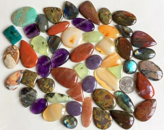 May include: Assortment of colorful gemstone cabochons in various shapes and sizes, including amethyst, agate, jasper, and labradorite. The cabochons are arranged on a white surface.