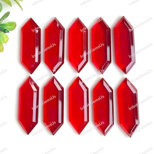 Puede incluir: Una colección de diez cristales de piedras preciosas de color rojo vibrante, cada uno con una forma hexagonal alargada única. Los cristales están dispuestos en un patrón de cuadrícula, mostrando sus superficies pulidas y bordes afilados. Ideales para joyería.