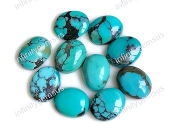 May include: A collection of oval-shaped turquoise gemstones with dark matrix patterns. The polished stones vary in shades of blue and green, with some displaying a spiderweb-like pattern. The gemstones are arranged on a white surface.