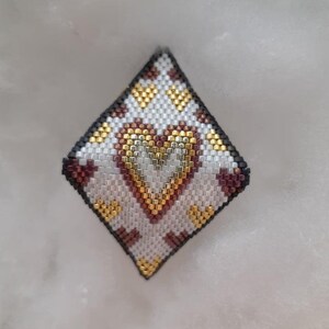 May include: A white, gold, and brown beaded heart-shaped pendant with a diamond-shaped design.