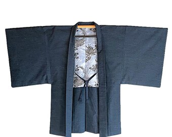 Op de afbeelding: Een donkerblauwe Japanse kimono met wijde mouwen. De binnenvoering heeft een wit en grijs drakenpatroon. De kimono is aan de voorkant open en vastgebonden met een donkerblauw koord.