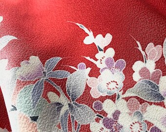 May include: A red fabric with a floral pattern. The flowers are white with pink and purple accents. The fabric has a textured surface.