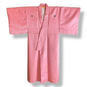 May include: A pink Japanese kimono with a white collar and a small black design on the front. The kimono is made of a silky fabric and has a traditional style.