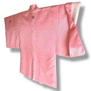 May include: A pink Japanese haori, a traditional short jacket, with a white lining and a subtle diamond pattern. The haori has a high collar and a decorative circle on the back.