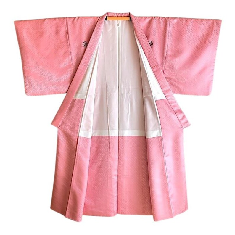 May include: A pink Japanese kimono with a white lining. The kimono is made of a soft, silky fabric and has a traditional design.