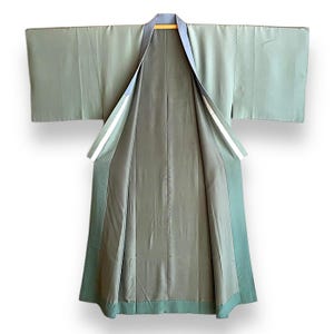 Puede incluir: Un kimono verde salvia con forro azul oscuro y ribete blanco. El kimono est&aacute; abierto y colocado plano, mostrando el forro y el interior de las mangas.