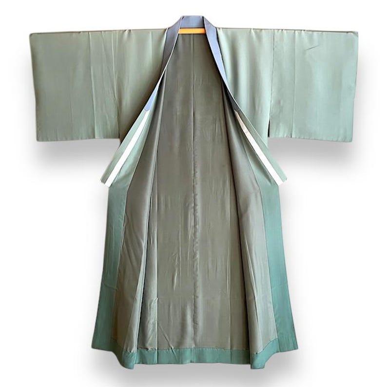 Puede incluir: Un kimono verde salvia con forro azul oscuro y ribete blanco. El kimono est&aacute; abierto y colocado plano, mostrando el forro y el interior de las mangas.