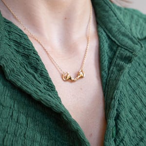 May include: A gold chain necklace with a small gold horse bit pendant. The necklace is worn by a person wearing a green shirt.