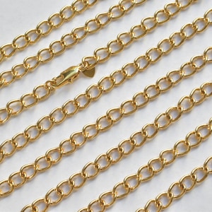 May include: A close-up of a gold chain necklace. The chain is made of small, oval-shaped links. The chain is lying flat on a white surface.