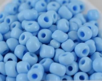 Puede incluir: Primer plano de un montón de cuentas de semillas de color azul claro en una bandeja triangular blanca.