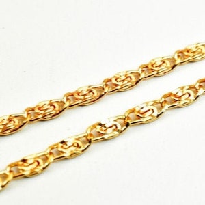 Op de afbeelding: Een gouden ketting met een touwachtig ontwerp. De ketting is gemaakt van kleine, met elkaar verbonden schakels die een textuur creëren.