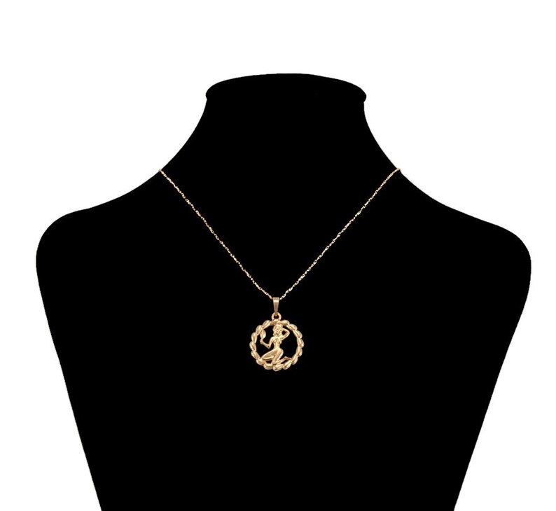 May include: A gold chain necklace with a pendant featuring a stylized figure of a woman. The pendant is round and has a detailed design.