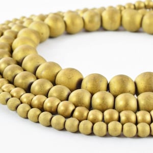 May include: A set of four strands of matte gold round beads. The beads are different sizes, with the largest beads in the back and the smallest beads in the front.